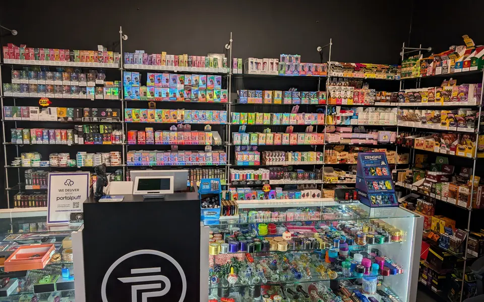 Inside Fancy Puffs: the counter, the vape wall behind it and a lit glass display case to one side.